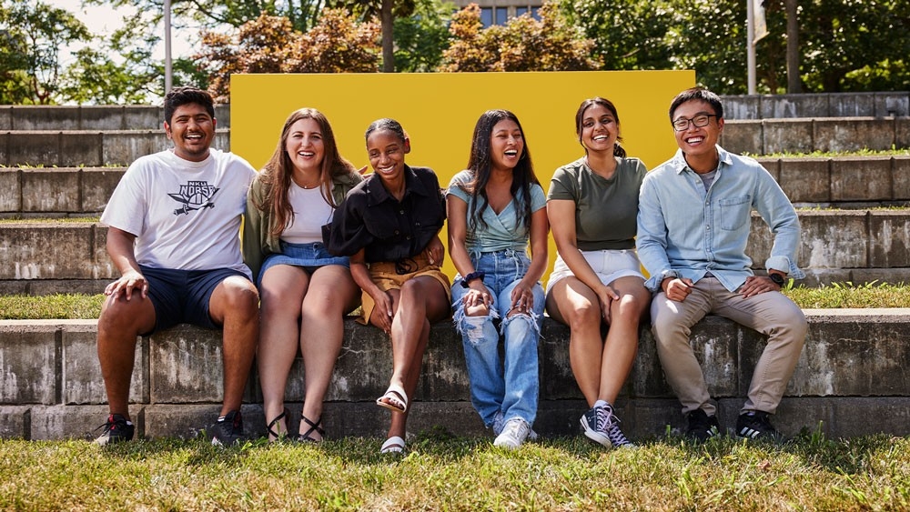 A group of six NKU students smile and laugh as they sit outdoors on NKU's campus.