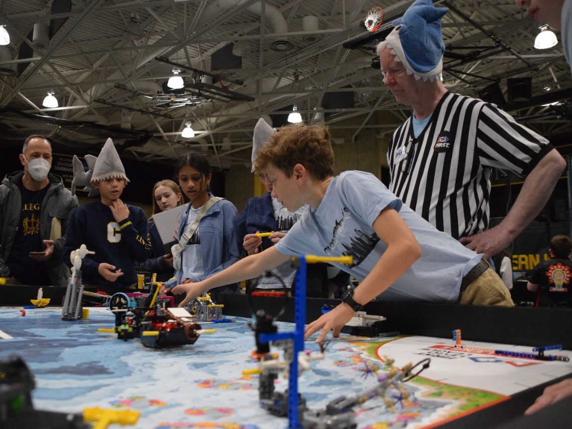 Middle school-aged kids wearing fun shark hats intently watch their team's LEGO robot perform at the annual Kentucky robotics competition at Northern Kentucky University.