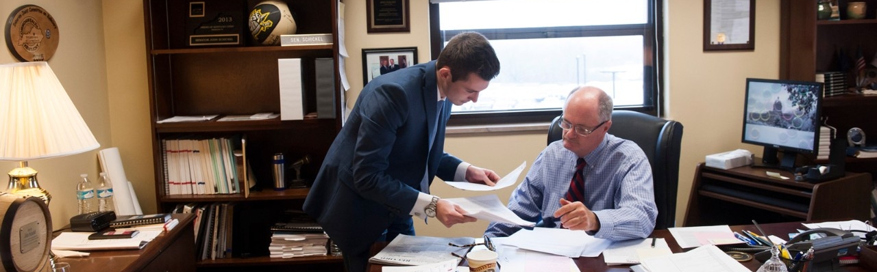 Two men dressed professionally, sitting in an office examining documents.