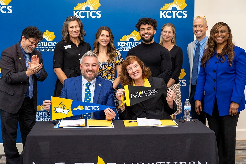 KCTCS and NKU officials pose at a table in front of a blue KCTCS back drop where they had just signed the subject agreement. 